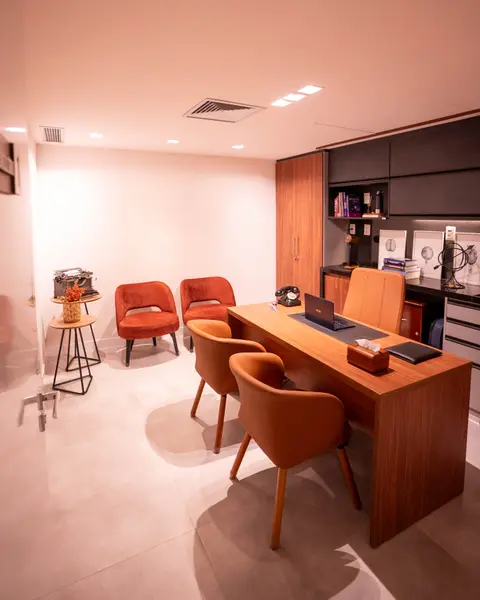 Consultório com mesa de madeira, cadeiras e estante
